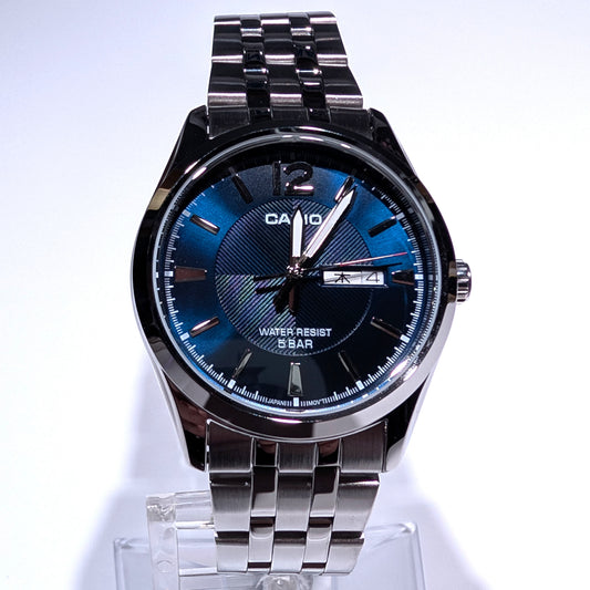 A Casio men's analog watch with a polished silver-tone stainless steel case and link bracelet, featuring a textured blue sunburst dial with silver-tone hands and markers.