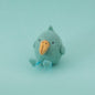 A small handmade felt bird toy in a light blue-green color with a contrasting orange beak, sitting against a solid light blue-green background.