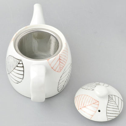 White ceramic teapot with leaf patterns on a gray background