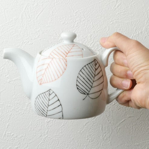 Ceramic teapot with leaf designs held by a hand against a light background