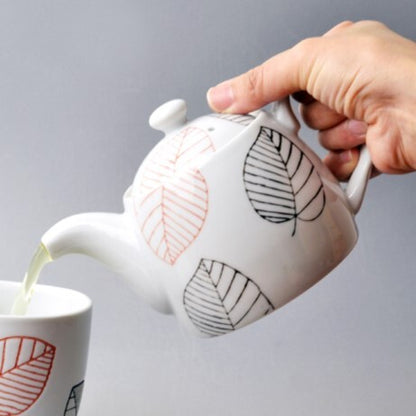 Ceramic teapot with leaf patterns being filled with tea into a matching cup.