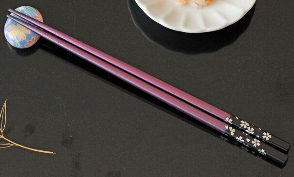 Purple chopsticks with black floral patterns on a dark surface