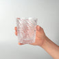 Hand holding a textured glass vase against a plain background