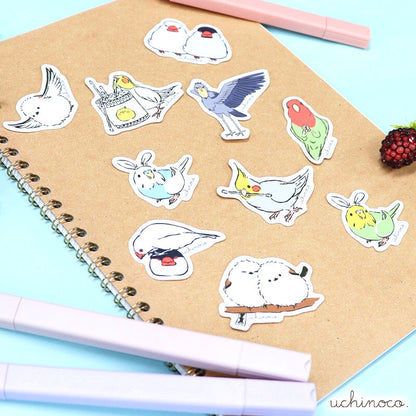 Set of colorful bird-shaped stickers on a notebook with pens and a small figurine.