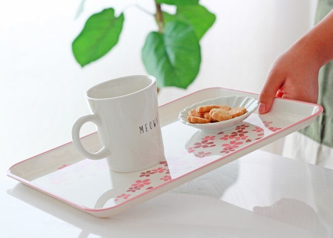 Person holding a tray with a mug and snacks on a white surface