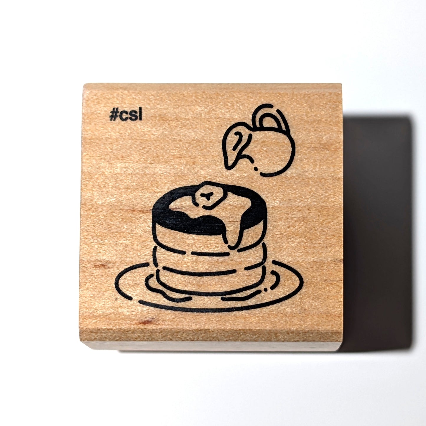 Wooden stamp with a design of a cake and the hashtag #cs1 on a white background
