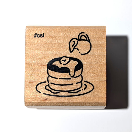 Wooden stamp with a design of a cake and the hashtag #cs1 on a white background