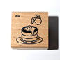 Wooden stamp with a design of a cake and the hashtag #cs1 on a white background