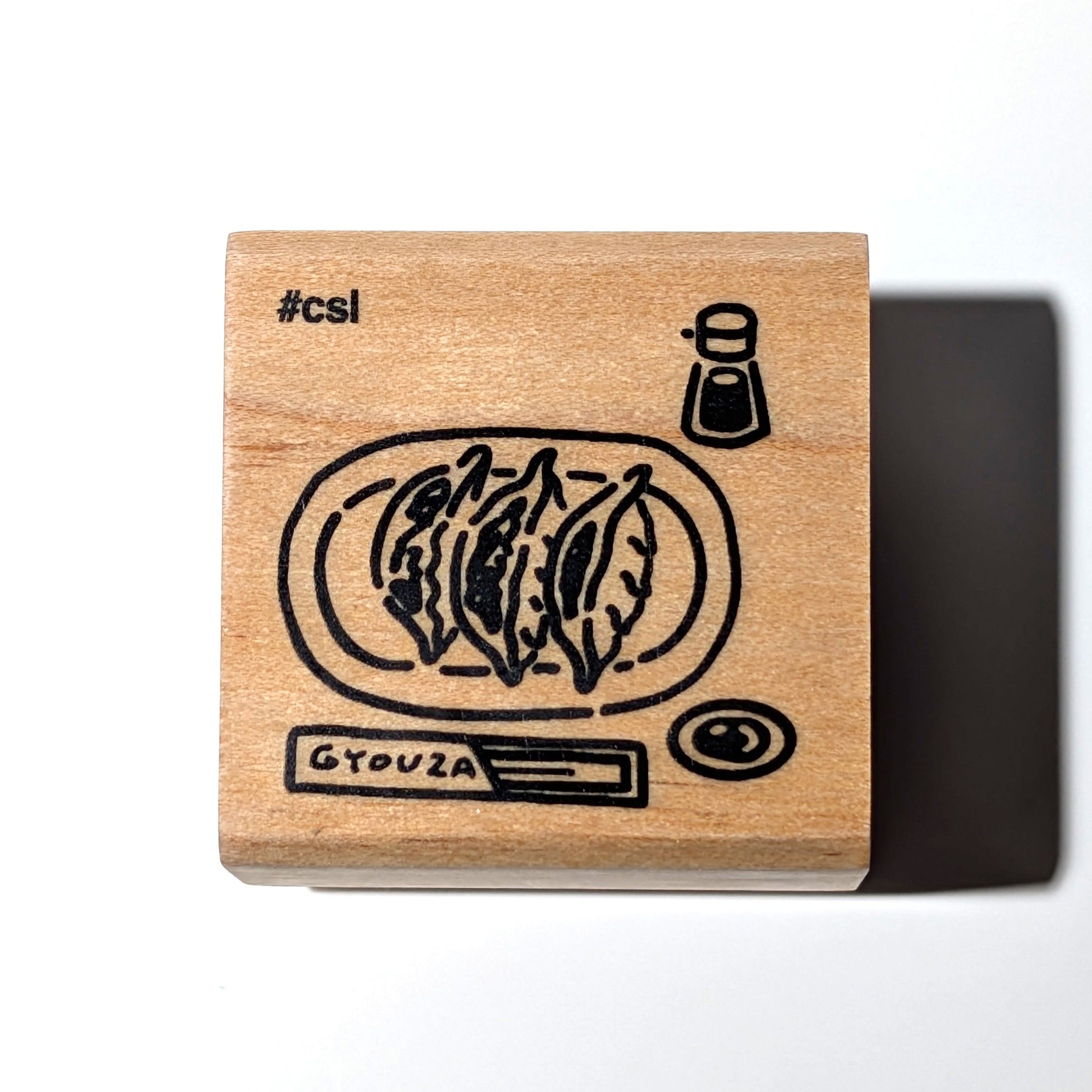 Wooden stamp with Gyouza illustration and '#csi' text on a white background