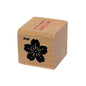 Wooden block with a black floral design and red text on a white background