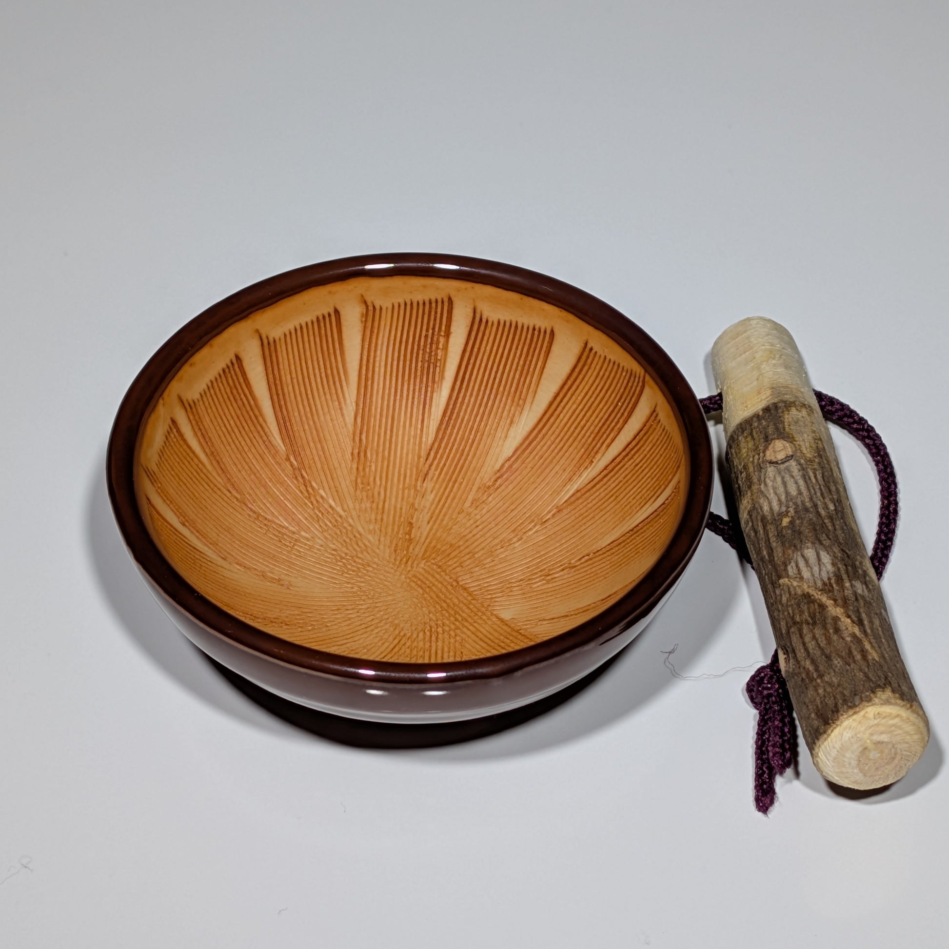 Wooden singing bowl with a wooden stick on a light gray background